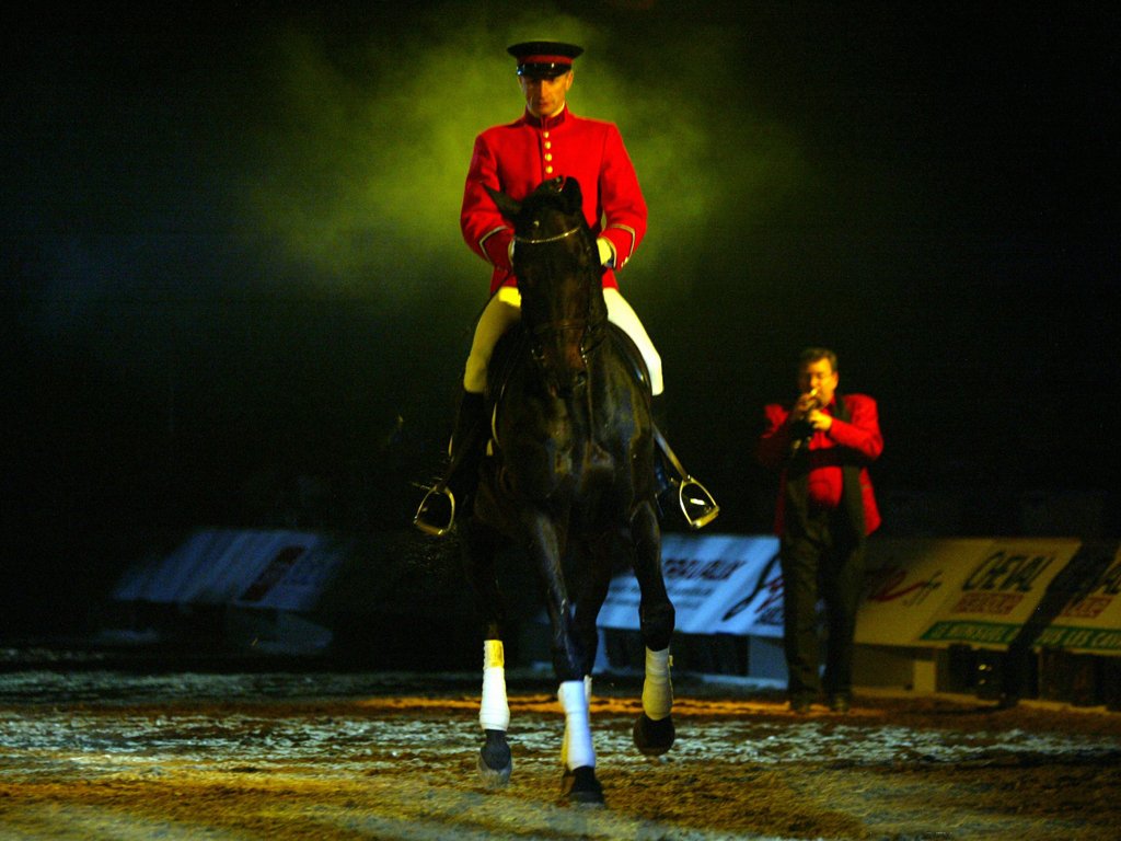 Un cavalier en habit rouge des Haras nationaux au trot dans la pénombre, lors d'un spectacle de Cheval Passion à Avignon