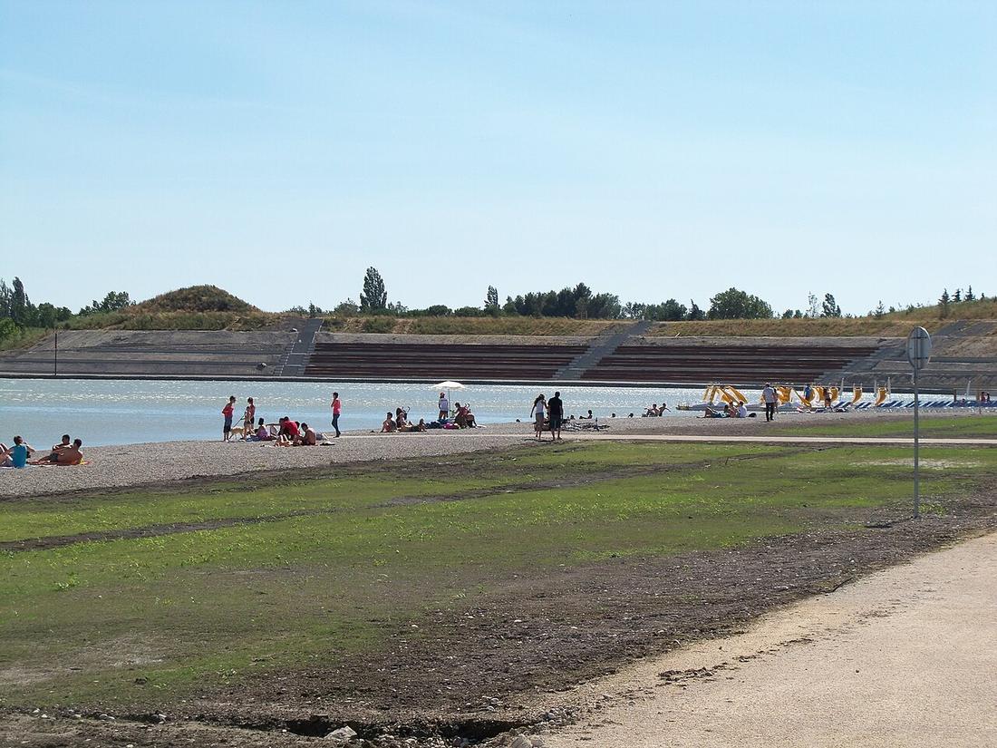 La plage de galets du lac de Monteux, avec des baigneurs et les gradins au fond